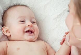 אמא רוכנת מעל תינוק מחייך