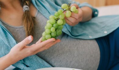 אישה בהריון שוכבת על המיטה ואוכלת ענבים