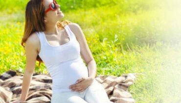 אישה הרה במשקפי שמש יושבת על העשב בשדה