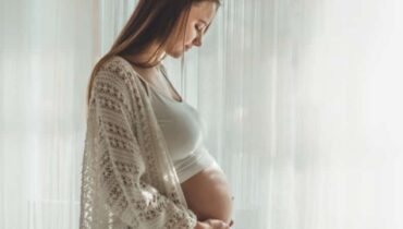 אישה מחזיקה את הבטן ליד החלון