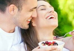 בחור חייכני יושב עם אישתו בפארק ומאכיל אותה עם פירות יער