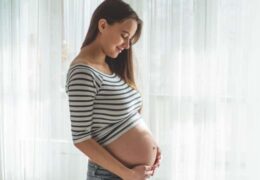 אישה בהריון ליד החלון מחזיקה את הבטן