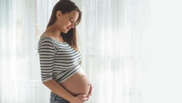 אישה בהריון ליד החלון מחזיקה את הבטן